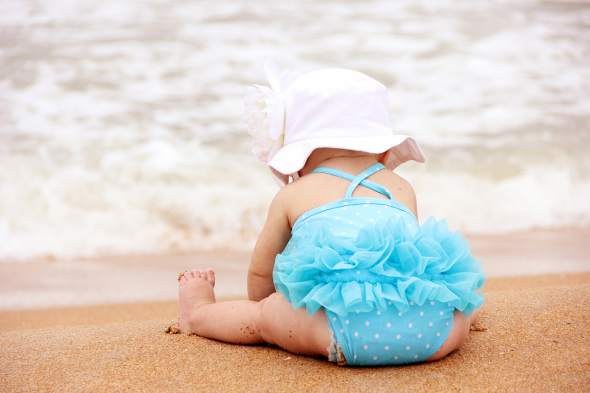 Baby sitting at beach wearing the beach essentials.